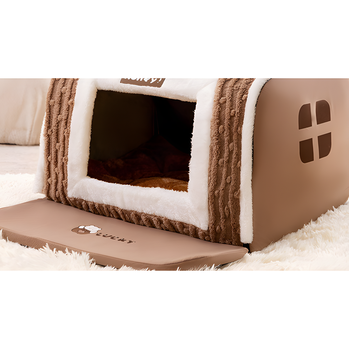 A brown and white house-shaped pet bed with a textured knit exterior, plush white trim, and a sliding door, shown on a white shag rug.