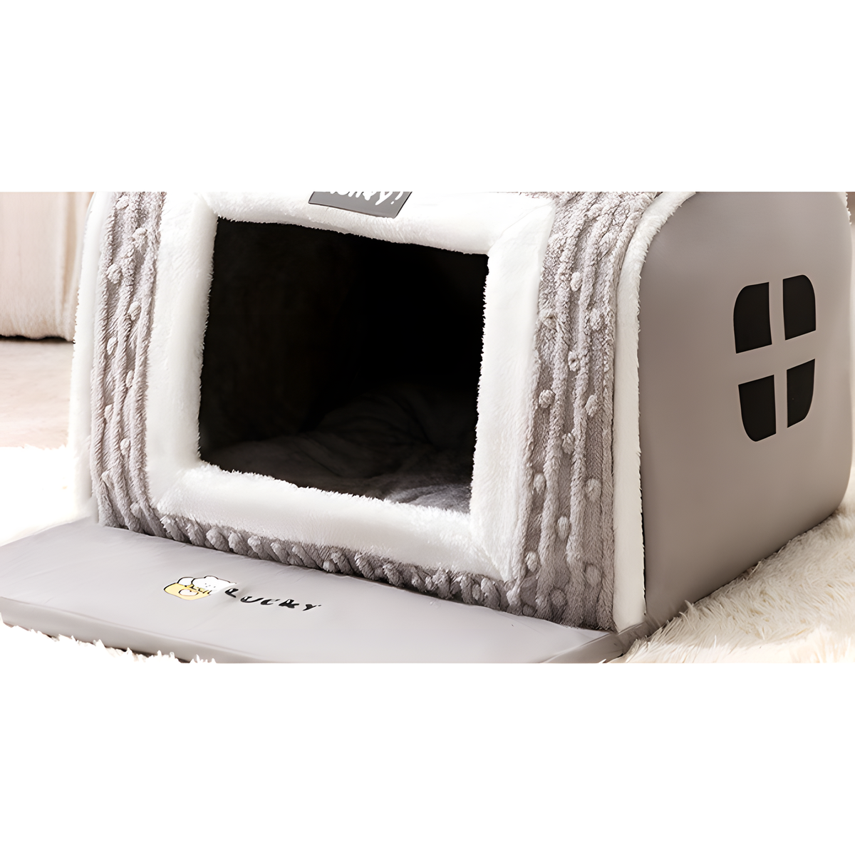 A gray and white house-shaped pet bed with a textured knit trim, shown on a white rug. The brand name 'KUKUI' is visible on the front panel.