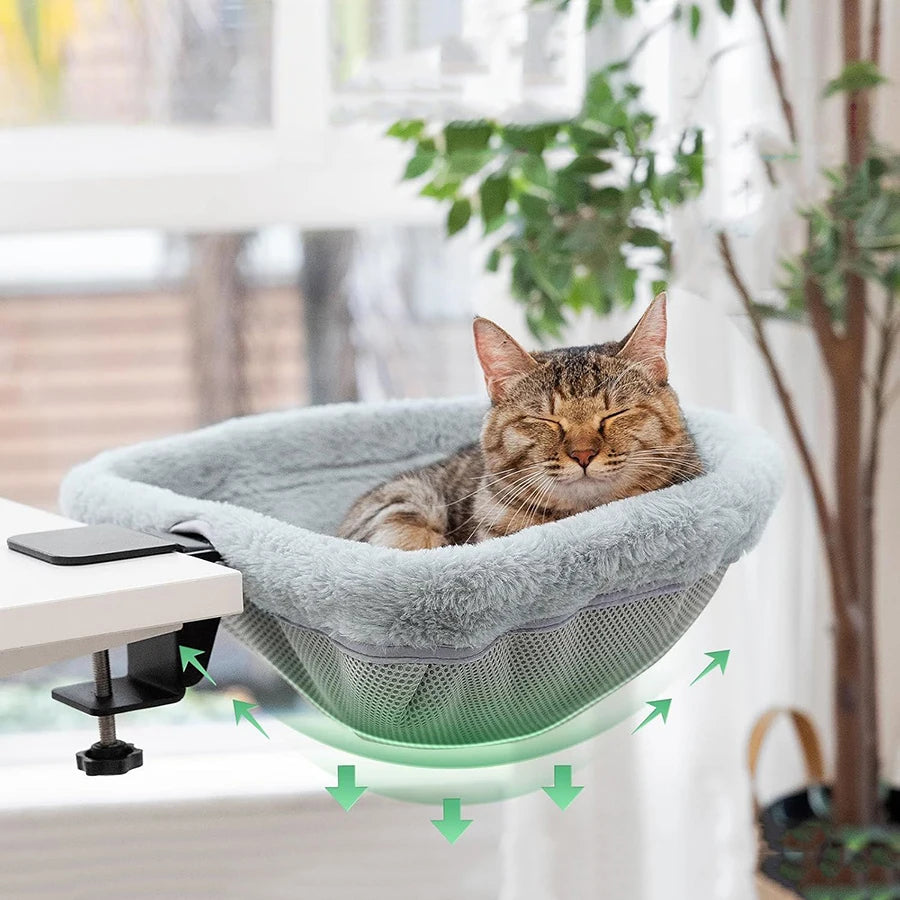 Cat lounging in a gray hammock attached to a desk with green arrows indicating support.