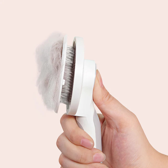 Hand holding a white grooming brush with bristles against a light pink background