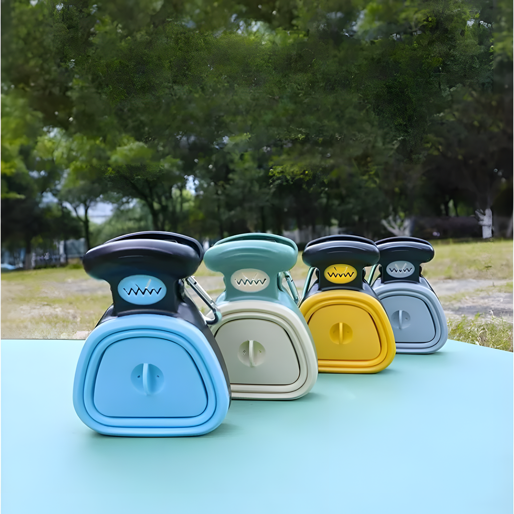 Four small plastic storage containers or organizers in assorted colors (blue, mint, yellow, and gray) with black lids, arranged on a light blue table outdoors with a blurred green park background.