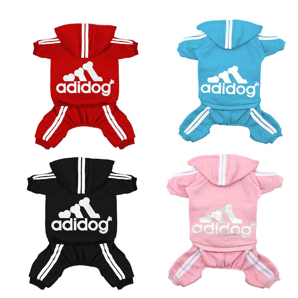 Four pet tracksuits shown in red, blue, black, and pink, each with a hooded sweatshirt and matching pants. Each outfit has white double stripes down the sleeves and legs, and a white 'adidog' logo printed on the front.